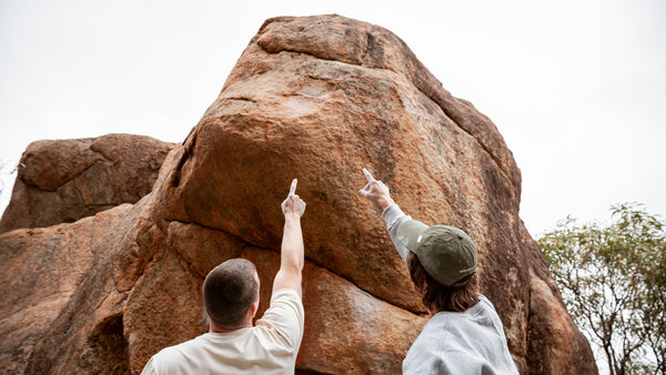 Two people pointing at a large rock formation with trees in the background