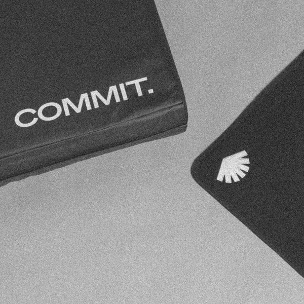 Black climbing pad with 'COMMIT.' text and white logo on a gray background