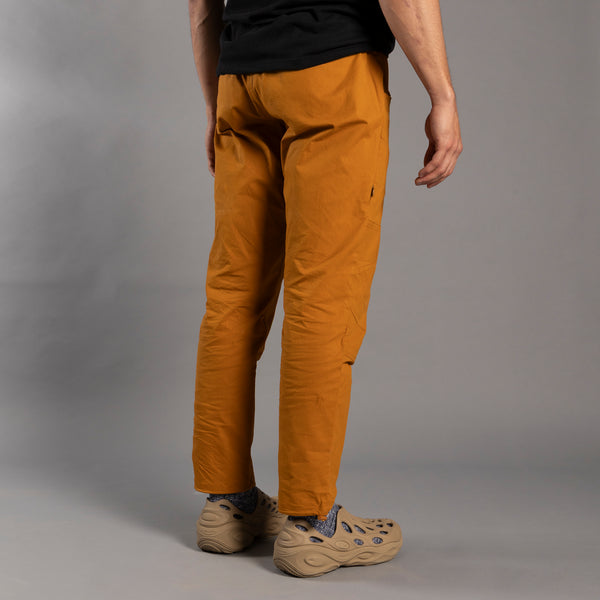 Person wearing mustard yellow climbing pants and beige shoes on a gray background