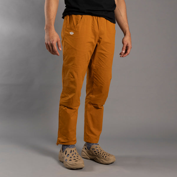 Person wearing mustard yellow climbing pants on a gray background