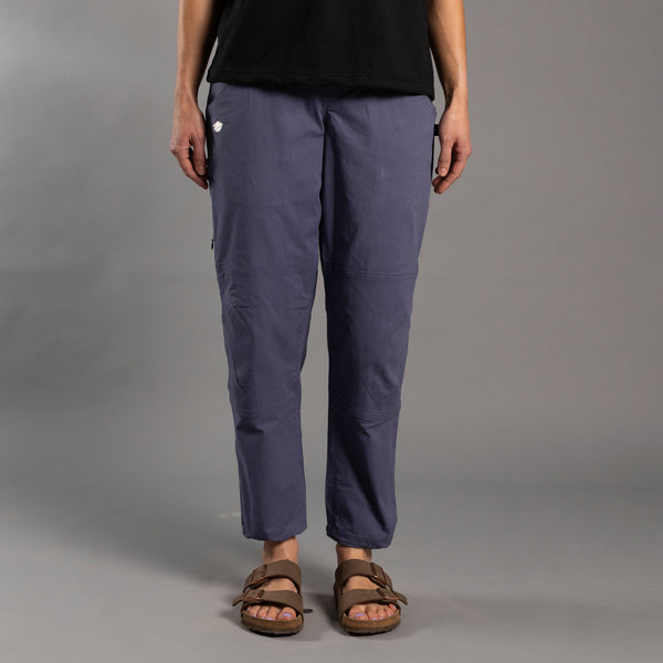 Person wearing purple climbing pants and brown sandals on a gray background