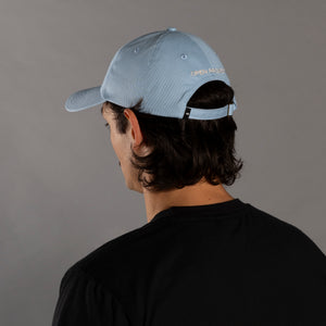Person wearing a light blue cap with a brand logo on the back against a gray background