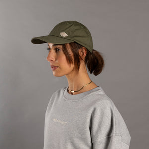 Woman wearing a green cap and gray sweatshirt with a logo on a gray background