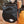 Black chalk bag with a logo, attached to a climbing harness, with a brush on top against a blurred natural background.