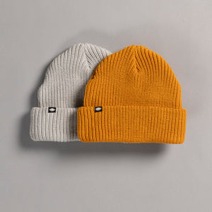 Two knit beanie hats, one gray and one mustard yellow, on a gray background.