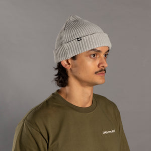 Man wearing a gray knit beanie and green sweatshirt against a gray background