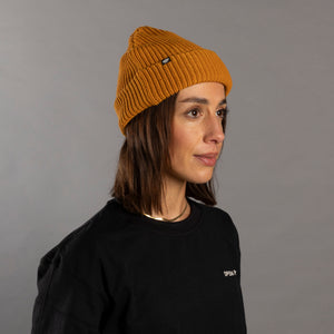 Person wearing a mustard yellow beanie and black sweatshirt against a gray background