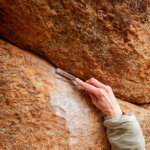 Hand holding a climbing brush against a rock surface