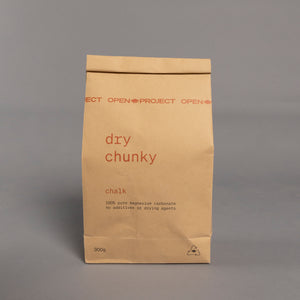 Brown paper bag of climbing chalk labeled 'dry chunky chalk' on a gray background
