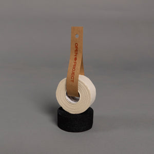 Roll of white climbing tape on a black roll of tape with a brown tag labeled 'Open Project' against a gray background