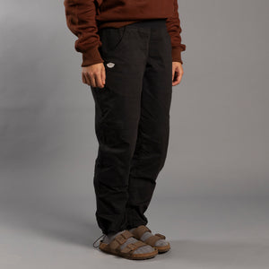 Person wearing dark climbing pants and a brown jacket on a gray background